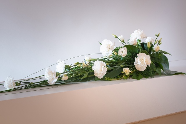 Enkel hvit blomsterdekorasjon oppå en hvit kiste.
