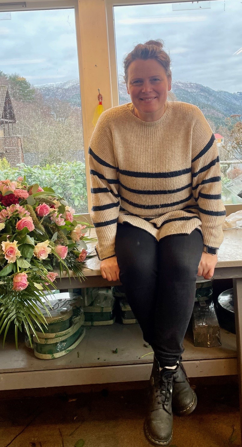 Floristen Irene Erdal sitter på en benk sammen med blomsterdekorasjonene sine.